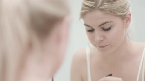Woman Applies Mascara in Front of Mirror