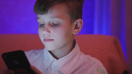 Boy Using Phone in Colorful Light at Home