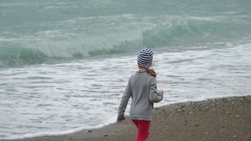Back View of Little Girl Walking Along Rough Sea