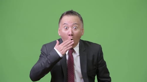 Mature Japanese Businessman Surprised Against Green Background