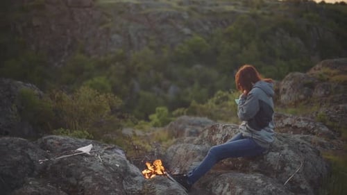 Woman Sitting by Fire in Nature Landscape
