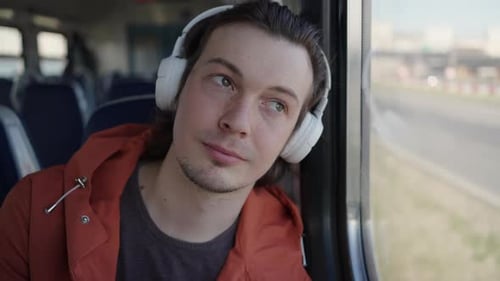 Man on Train Looking Out Window Wearing Headphones