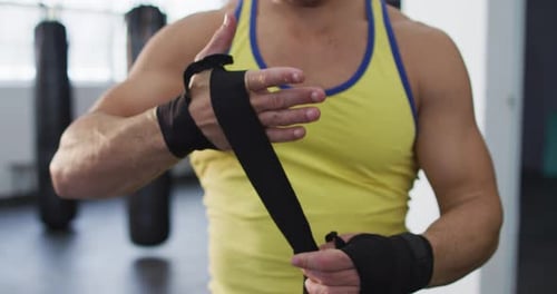 Mid section of caucasian male boxer wrapping boxing tape on his hands at the gym
