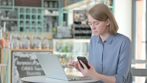 Young Woman Working on Smartphone and Laptop in Cafe