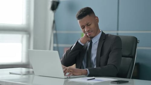 African Businessman having Neck Pain while using Laptop in Office