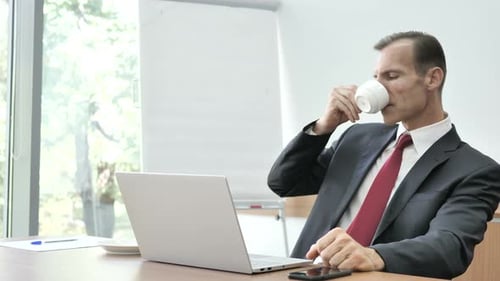 Man in Suit Works at Laptop, Drinks Coffee
