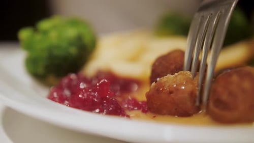 Close-up of plate with meatballs, broccoli , rice and jam. Person in cafe.