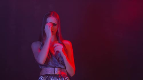 Woman in Shiny Outfit Poses Under Red and Purple Lights