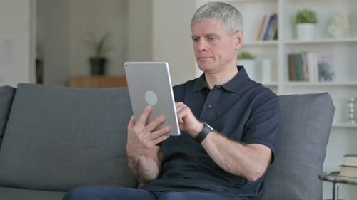 Mature Adult Using Silver Tablet Indoors on Sofa