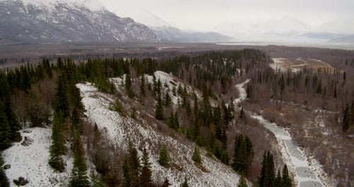 Aerial helicopter shot, fly over rocky, snow Alaskan mountainside to see more mountains in distance,