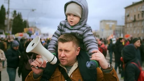 Father Carries Child with Megaphone in Urban Crowd