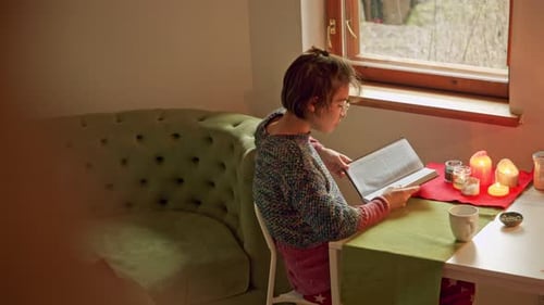 Woman Reading Book at Table by Window