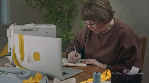 Woman Taking Notes While Sewing at Home