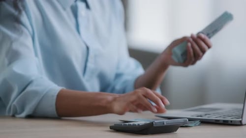 Person Counting Money at a Desk with Laptop