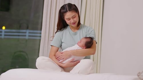 Mother Cradling Newborn Infant in Bedroom