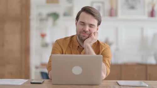Tired Young Man taking Nap While Sitting in Office with Laptop