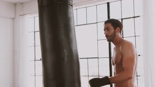 Shirtless Man Training with Punching Bag in Gym