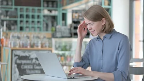Woman Typing on Laptop with Headache in Cafe