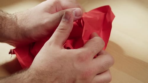 Hands Crushing a Red Paper Sheet Ball