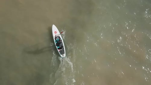 Birds eye view of a young man stand up paddle-boarding in the sea.