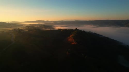 4K aerial view over mountain at sunrise in heavy fog. golden morning sunlight