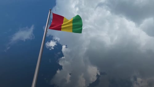 Waving Flag of Guinea on Flagpole in Cloudy Sky