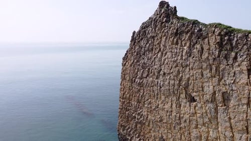 An unusual rock standing in the sea. Flat rock in the form of a sail with a hole in the middle