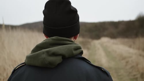 Junger Mann geht auf Landstraße. Wind schüttelt das trockene Gras
