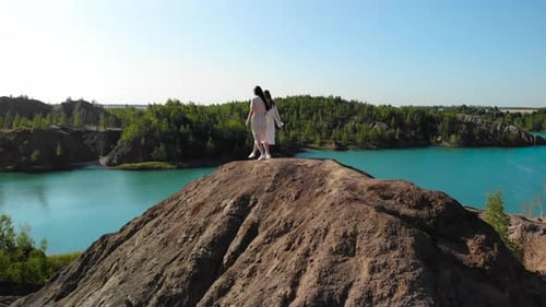 Incredible View of Two Women Who Meet at Top of Mountain Against Background of Blue Lake on the Edgr