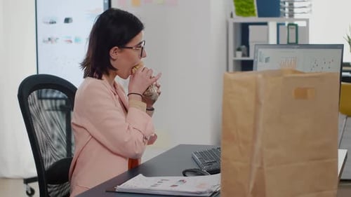 Geschäftsfrau isst einen Bissen leckeres Sandwich und trinkt Kaffee vor dem Monitor