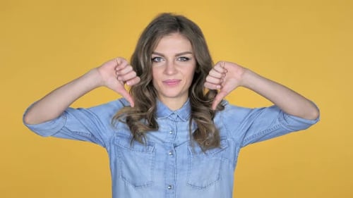 Young Girl Gesturing Thumbs Down Isolated on Yellow Background