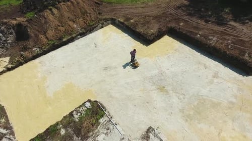 Homme travaillant avec un compacteur à plaques vibrantes dans la fosse de fondation d'une nouvelle maison sur un chantier de construction