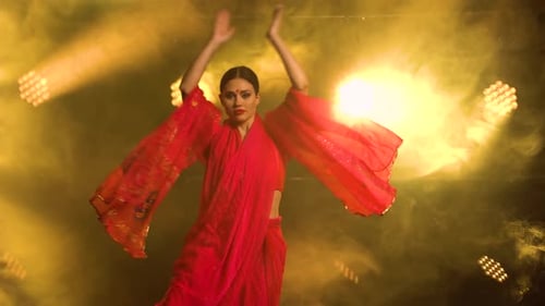 Une jeune fille danseuse dans un sari rouge dans une danse folklorique indienne sur scène dans un studio sombre avec de la fumée et