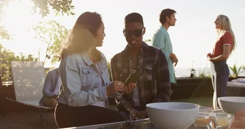 Friends Gather at Sunny Outdoor Party, Look at Phone