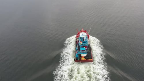 Traditional fishing boat with foamy wake sailing towards the endless horizon, birds eye view, aerial