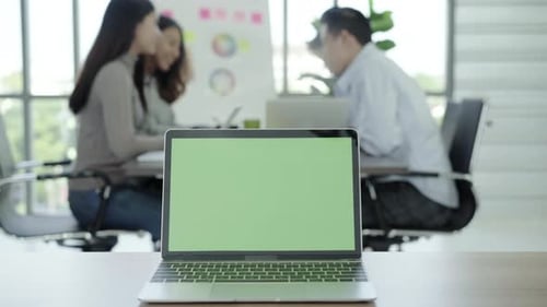 Laptop computer with green screen on table in office
