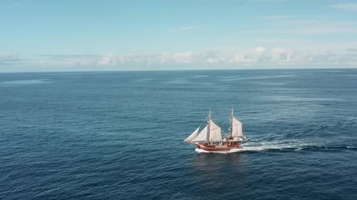 Um velho navio pirata solitário com velas brancas desliza sobre as ondas em mar aberto em dias claros