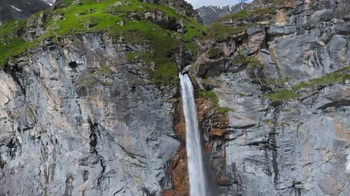 Aerial slow motion: drone flying over scenic high waterfall, mountain stream falling from cliff