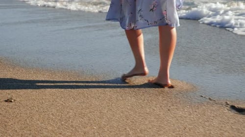 Woman walking on sandy beach at sunset.