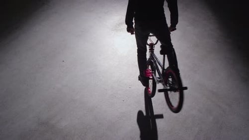 BMX rider doing tricks in dark warehouse.