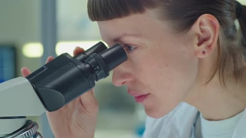 Female Scientist Viewing Sample Through Microscope in Laboratory