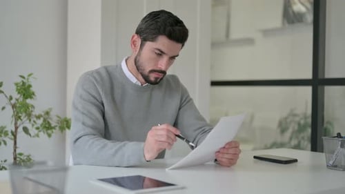 Young Man Reading Documents While Sitting in Office