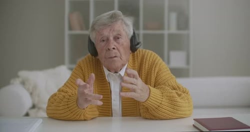 Grandmother 80 Years Old I'm Looking at the Camera Talking While Sitting in Headphones