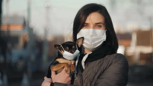 Woman in Protective Face Mask with Small Dog Wearing Medical Mask Too