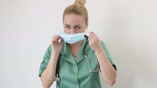 Portrait of Young Adult Female Doctor in Green Doctor's Coat Puts on a Medical Mask