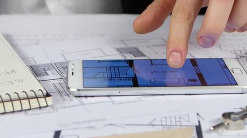Businessman Looks at Blueprints and Graphics in the Phone. Close Up