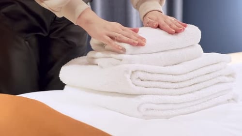 Hand Places Fluffy White Towels on Bed