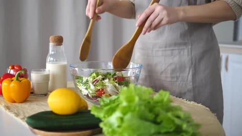 Person Mixing Salad in Kitchen with Wooden Spoons