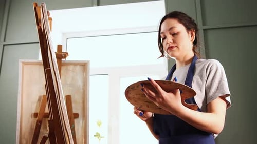 Art Studio Young Woman Choosing a Brush and Painting on Canvas