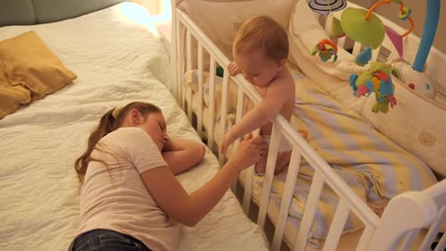 Baby in Crib Next to Sleeping Adult